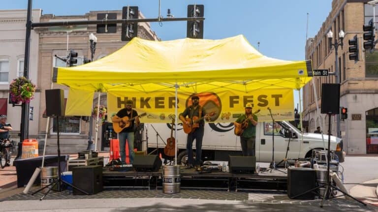 3 person band on a stage in front of a yellow Hiker Fest banner